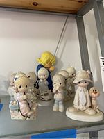 Wide view of eight child figurines including a child holding Christmas lights and others in prayer poses with various accessories.