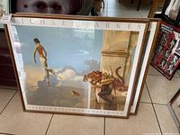 Two Michael Parkes art prints with wood frames and separating glass leaning on floor.