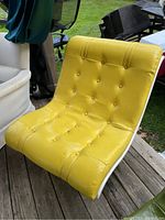 Full view of yellow vinyl button tufted scoop chair on wooden deck showing curved acrylic frame and scoop shape