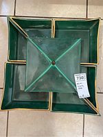 Top-down view of five green ceramic serving dishes with gold trim arranged on a wooden tray, one dish inverted in the center showing its underside.