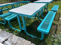 Full view of rectangular metal picnic table with turquoise frame and white tabletop outdoors on grass near stone edge