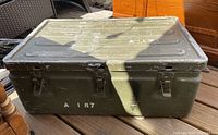 Front view of the olive green military foot locker trunk showing enclosed lid, metal clasps, and white stencil marking 'A 187'.