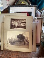 Stack of vintage black and white photographs on cream backing, with some framed items behind, showing water damage and discoloration.