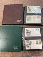 Photo showing a brown and a green binder both labeled 'First Day Cover' containing plastic sleeves with collectible first day cover stamped envelopes.