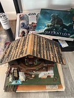 Top-down photo showing vintage German mechanical cottage with detailed roof and miniature figures inside, with Star Wars Illustration book and mug set box in background.