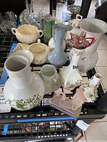 Wide view of assorted teacups, pitchers, vases in various shapes, colors, and brands on a black metal display shelf.