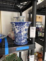 Photo of blue and white porcelain vases including a large wide vase with scenic floral design and other smaller vases behind it