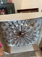 Full view of wall decor in its packaging showing starburst metal rods with glass discs at the tips.