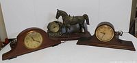 Wide shot of the lot showing two wooden mantle clocks and one cast horse desk clock on wooden base.