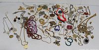 Lot of assorted costume jewelry including necklaces, brooches, earrings, bracelets displayed together on white background.
