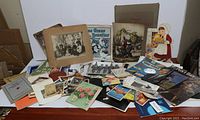 Wide view of the collection showing assorted vintage photos, sheet music, postcards, and ephemera spread out on a table.