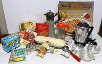 Overview of full lot showing all kitchen items including boxed Dansk pizza stone set, crystal carafe, Snoopy shakers in box, red handled ice scoop, Tang pitcher, glass bowls, salt and pepper shakers, cookbooks, and novelty items.