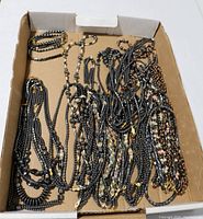 Top-down view of a cardboard box filled with multiple hematite bead necklaces and bracelets, showing variety in designs and sizes.