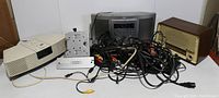 Photo showing slightly yellowed Bose Wave Radio, silver Teac cassette deck, vintage Tonfunk radio with wood trim, cassette adapter, and tangle of cables