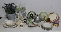 Wide view of the entire lot displaying decorative and functional vintage pieces: porcelain plates, teapots, flower frog, candleholders, sauce boat, bell and artificial lavender.