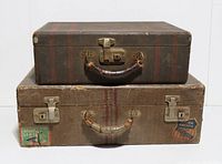 Photo of two vintage fabric-covered suitcases stacked, showing worn fabric, metal locks, and red stripes, with visible railroad and Pan Am stickers on the front sides.