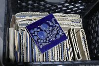 Crate with multiple vintage cobalt blue ceramic tiles wrapped in paper, one tile showing detailed raised floral and fruit pattern.