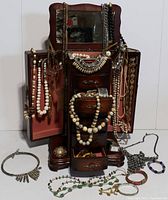 Full view of wood jewelry box open with jewelry displayed hanging and in drawers, showing necklaces and bracelets.