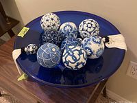 Top view showing the blue glass bowl filled with eight blue and white patterned ceramic decorative balls and two white tassels on edges.