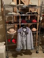 Full view of metal rack holding a variety of hats and a blue suede ladies coat hanging on the front