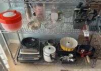 Wide angle of shelving rack with assortment of kitchen tools, pans, pot, juicers, cookie trays, and knife block visible.