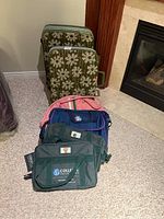 Photo showing two vintage Samsonite hard case suitcases with green and white floral patterns, and four soft duffel bags with different colors stacked together on carpet