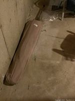 Patio umbrella inside a brown fabric storage case resting on a basement floor near a concrete wall.