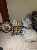 Overall view of assorted pillows, folded linens, afghan blanket, and towels on basement floor next to sofa