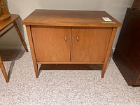 View of the wooden cabinet table showing both doors and metal pulls, standing on tapered legs.