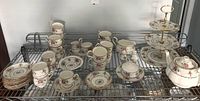 Full tea set arranged on metal shelving including cups, saucers, teapot, and stand.