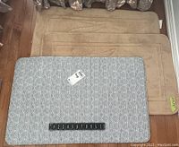 Three small area rugs stacked, two with alligator motif and one tan rectangular rug with pattern