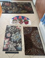 Photo showing all four rugs on tiled floor including three square rugs with floral patterns and one half-round white floral rug