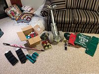 Full view of golf caddy, golf balls in box, hats, rags, weights, and umbrella laid out on carpet near couch.