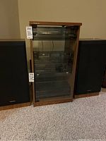 Front view of Technics stereo cabinet stand with glass door and magnet latch, flanked by stereo speakers.