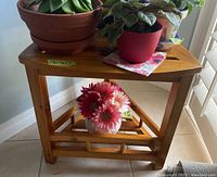 Triangular light-stained wood table shown with several potted plants on top and lower shelf, illustrating dimensions and structure.