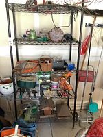 Full view of black metal shelf holding assorted garden and hand tools including saw, basket of tools, gloves, bird houses, and garden accessories.