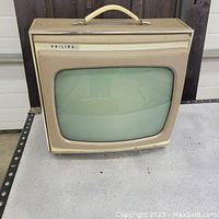 Front view of the vintage 1950s Philips portable television showing curved screen and beige casing with carry handle.