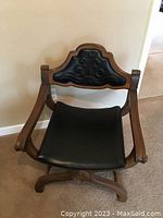 Front view of the 1970s Savaranola chair showing black leather seat and backrest with carved wood frame.
