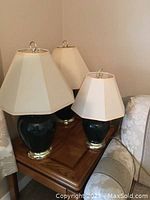 Three black table lamps with white hexagonal shades on a wooden side table in a corner between an armchair and a sofa.