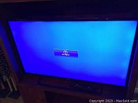 Front view of the TV screen turned on but showing 'No Signal' message, remote control placed on stand below it