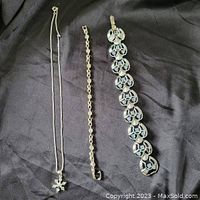 Three silver tone jewelry pieces laid out on black fabric background.