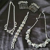 Full view of 3 necklaces, 1 bracelet, and 2 hair combs, all silver-tone with clear rhinestones in floral and geometric designs.