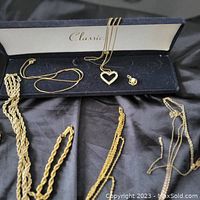 Overall view of multiple gold-tone necklaces and a heart-shaped rhinestone pendant charm with a small clasp in a jewelry box on black fabric