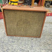 Front view of Crescendo amplifier showing woven speaker cloth grille and wooden reddish-brown cabinet with handle on top.