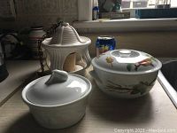 Wide shot showing all three items: the white ceramic lantern or candle holder with hanging chain, a plain white covered sugar bowl, and a fine china lidded bowl with fruit and floral design.