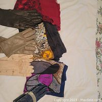 Photo showing several pairs of gloves in black, beige, and blue on scarves with floral patterns and solid red color.
