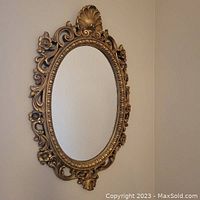 Side view of large ornate oval mirror with detailed gold tone resin frame featuring floral and shell accents.