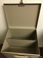 Top open view of small metal file cabinet showing inner divider for document separation, beige color.