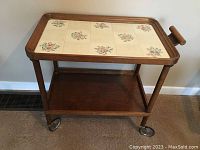 Full view of the wooden bar cart with tiled top, lower wooden shelf, and wheels for mobility.