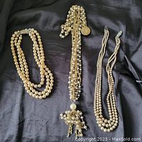 Four faux pearl necklaces displayed on a black fabric background showing varied lengths and styles, including a long tassel necklace.